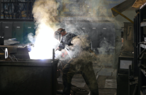 Welder in Shop Surrounded by Weld Fume